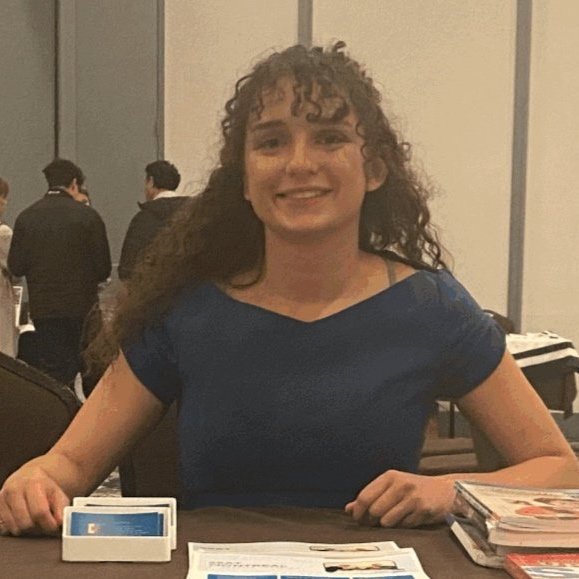 a female student in a red and black graduation outfit standing outside smiling