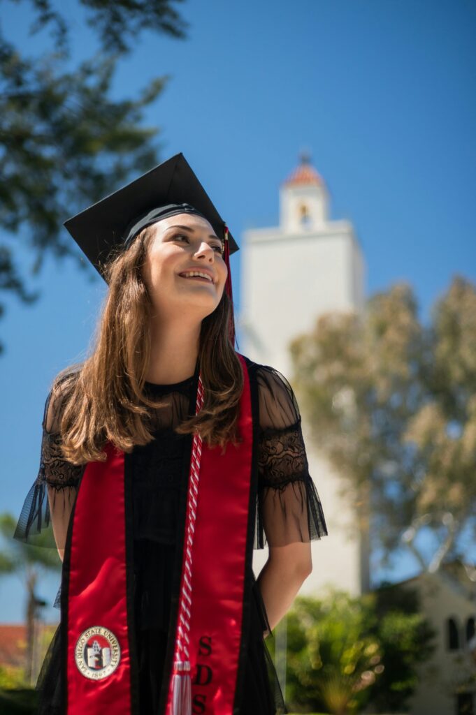 a female student in a red and black graduation outfit standing outside smiling